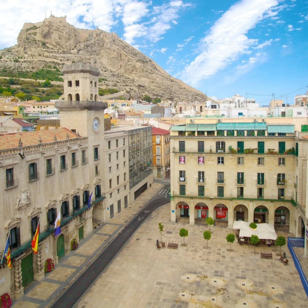 Plaza hist&oacute;rica con edificios y reloj, vista a la monta&ntilde;a al fondo.