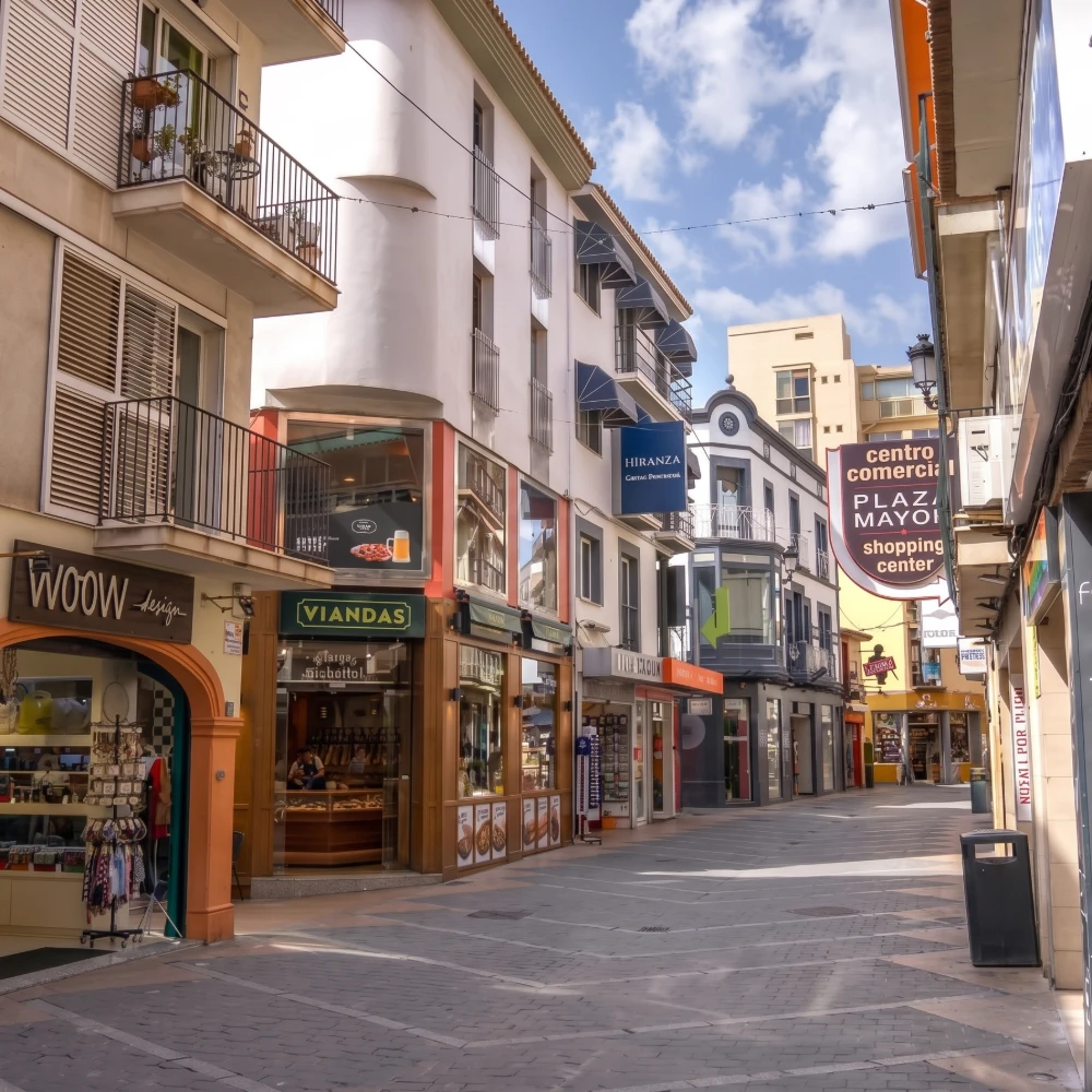 Calle comercial con tiendas, letreros &ldquo;Centro Comercial Plaza Mayor&rdquo; y balcones