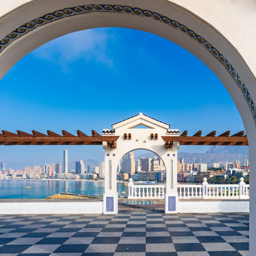 Arco con azulejos sobre terraza con vista al puerto y rascacielos al cielo azul