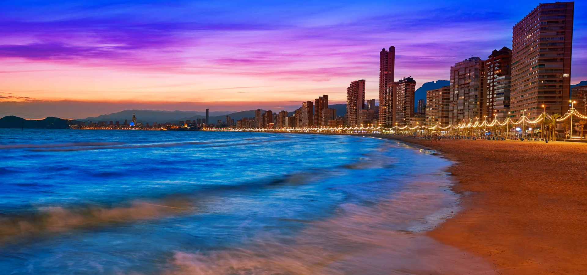 Atardecer en playa con edificios y luces sobre el paseo costero