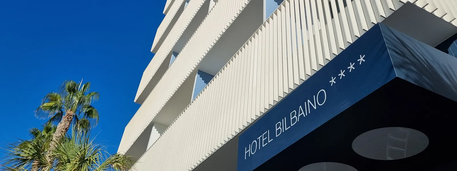 Fachada del Hotel Bilbao con cartel azul y palmeras bajo cielo despejado