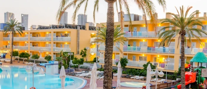 Hotel con piscina y palmeras al atardecer.