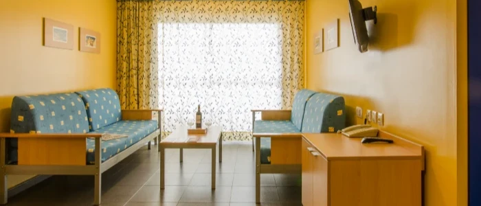 Sala de estar con dos sof&aacute;s azules y escritorio, con ventana al centro.
