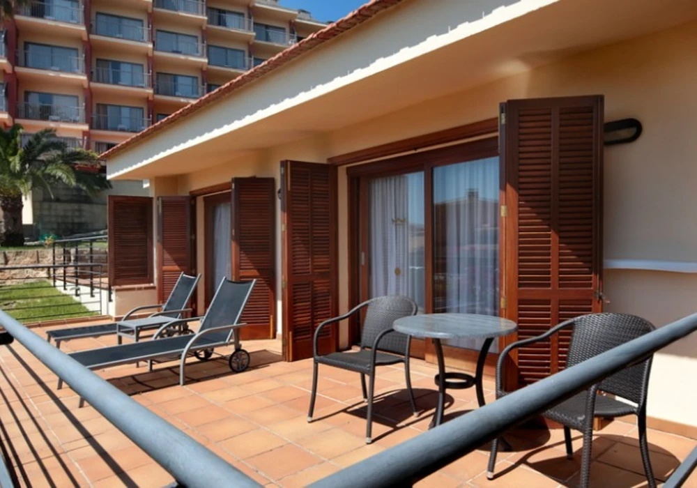 Terraza con mesas, sillas y puertas con persianas en un hotel/apartamento.