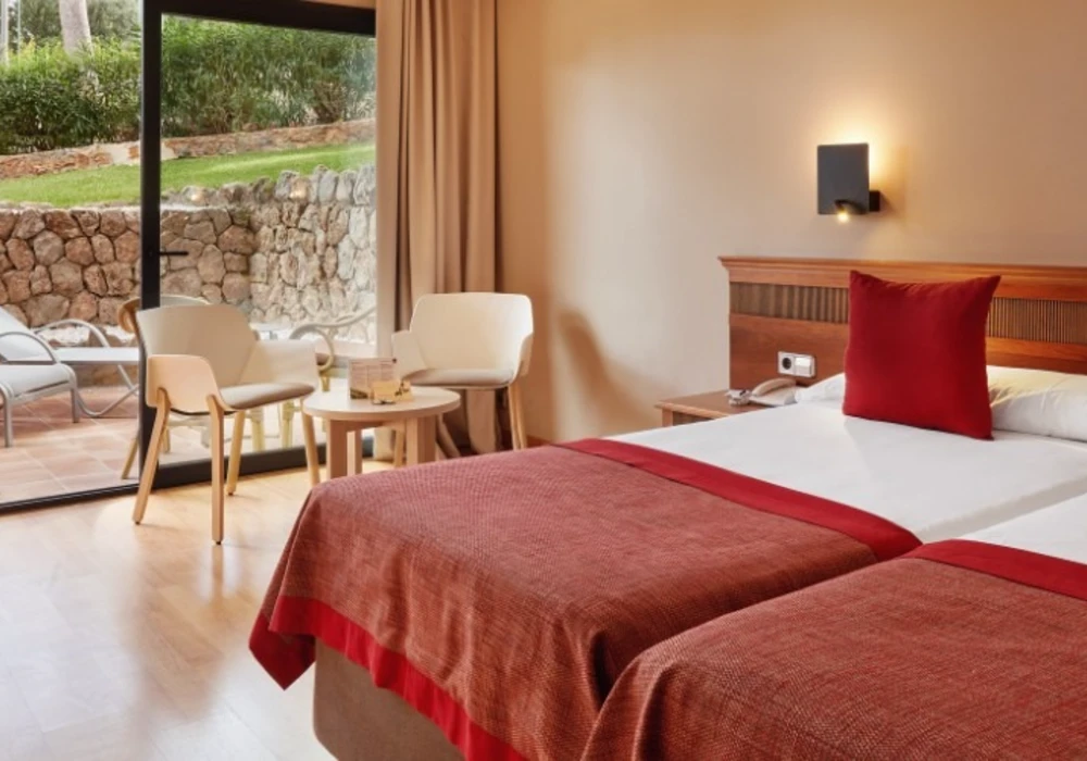 Habitaci&oacute;n con cama doble, cojines rojos y vista al jard&iacute;n desde la terraza