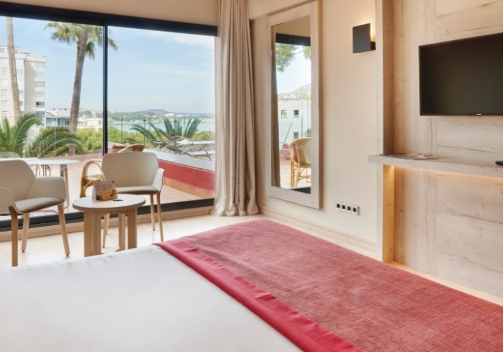 Habitaci&oacute;n de hotel con cama, cortinas, terraza y paisaje al fondo.