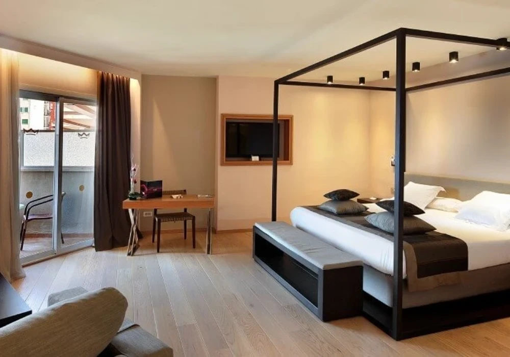 Habitaci&oacute;n de hotel moderna con cama grande, escritorio y balc&oacute;n.