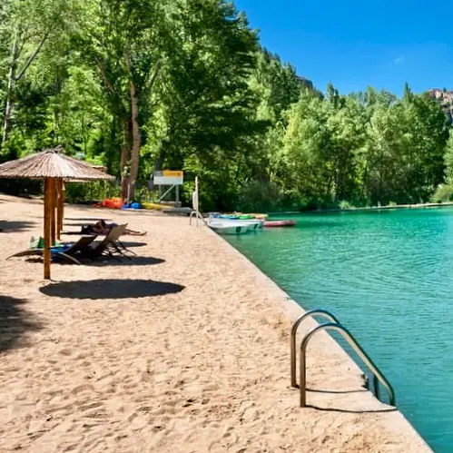 Playa con tumbonas y escaleras al agua, junto a un río rodeado de árboles.