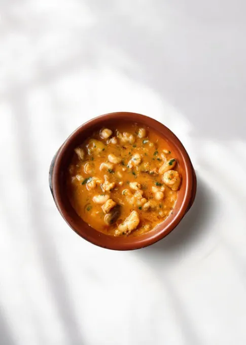 Taz&oacute;n de sopa naranja con trozos de pollo y hierbas frescas.
