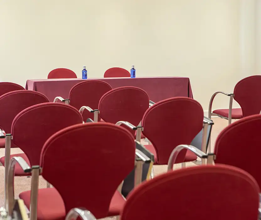 Sillas rojas de auditorio con mesa y botellas en el centro