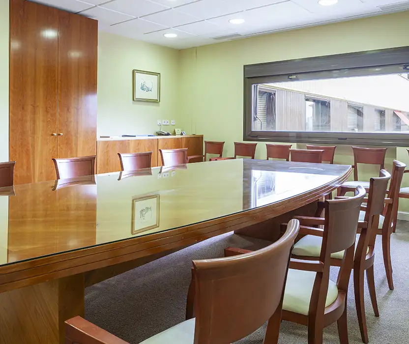 Sala de reuniones con mesa larga y sillas de madera, luz natural por ventana
