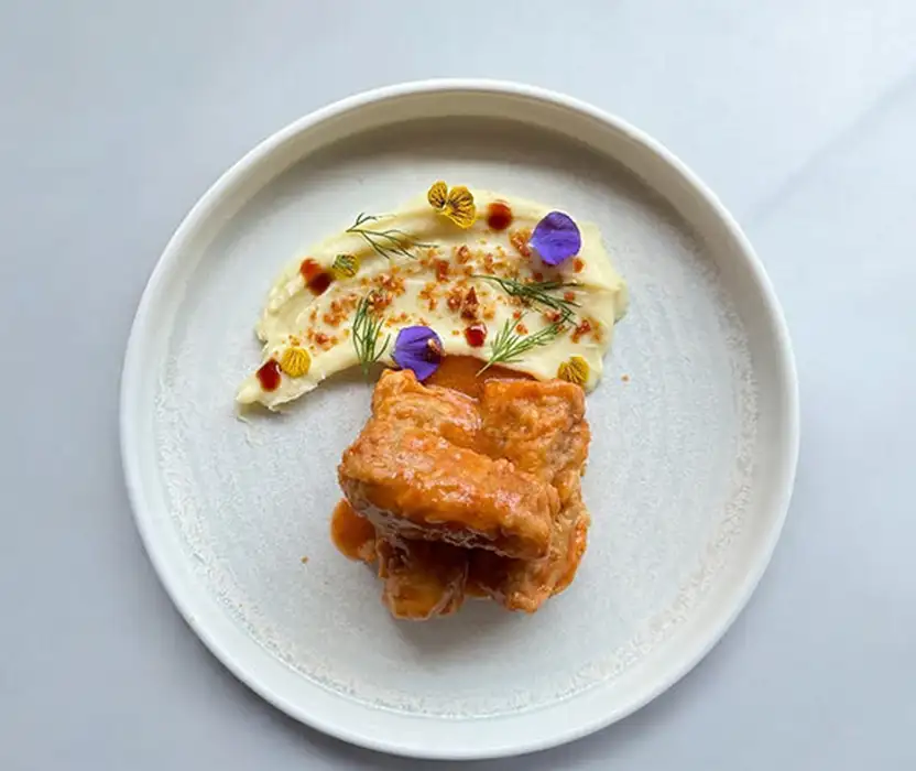 Plato con porci&oacute;n de salm&oacute;n, pur&eacute; cremoso y aceite con hierbas y brotes morados.