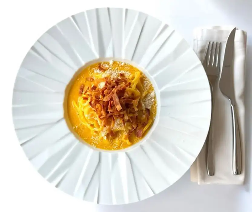 Plato con crema amarilla y toppings, con cubiertos al lado.