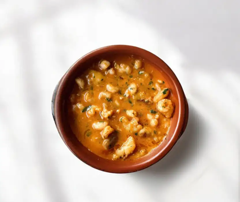Taz&oacute;n de sopa de tomate con trozos de pollo y hierbas, sobre fondo blanco