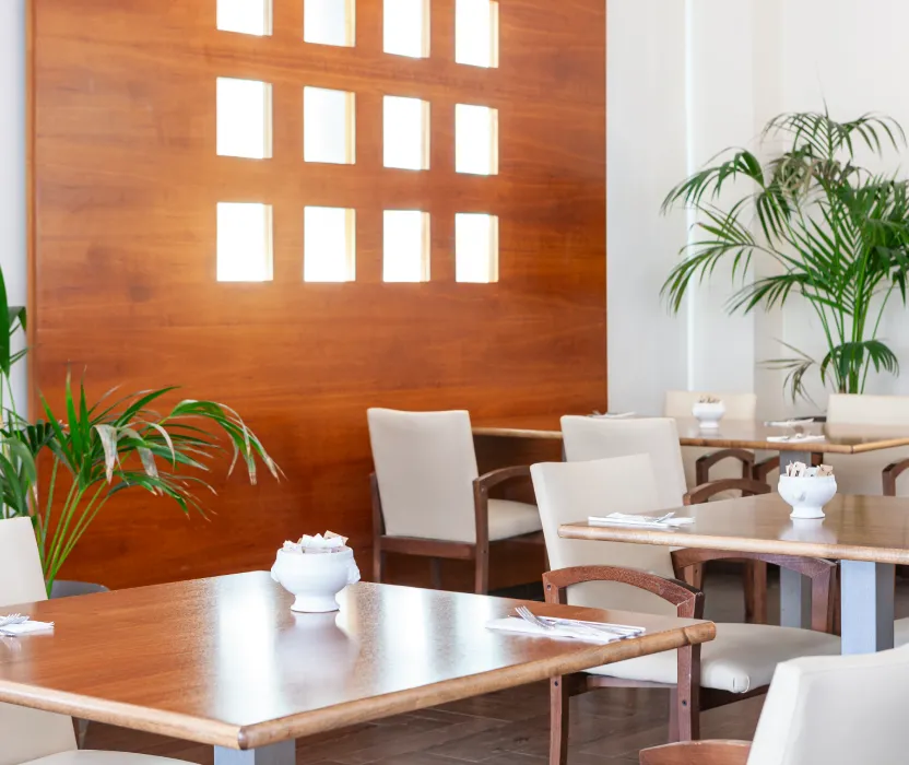 Sala de reuniones con mesas de madera, sillas blancas y plantas decorativas.
