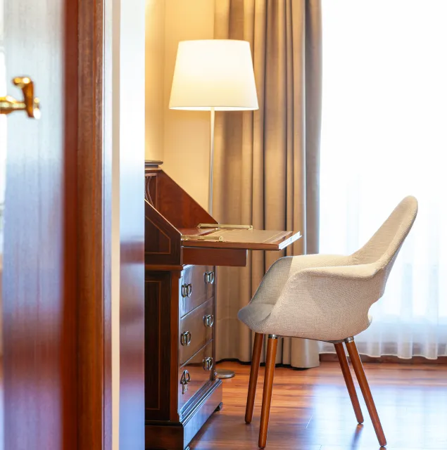 L&aacute;mpara y escritorio de madera con silla tapizada junto a la cortina
