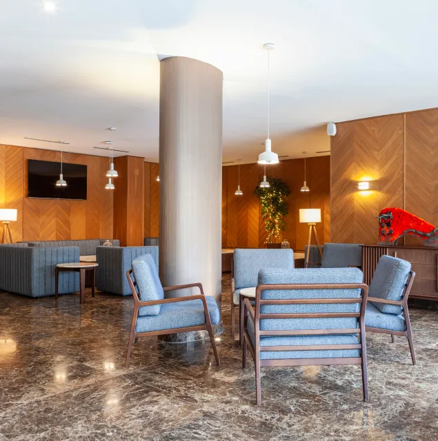 Lobby moderno con sillones azules, columnas y luces colgantes.