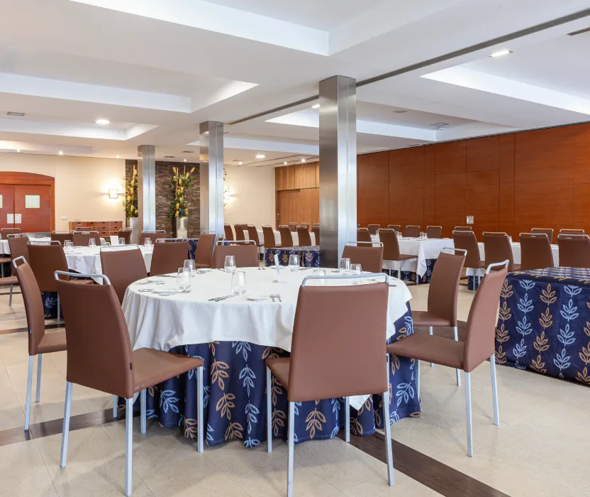 Sala de banquetes con mesas, sillas y mantel azul con flores blancas.