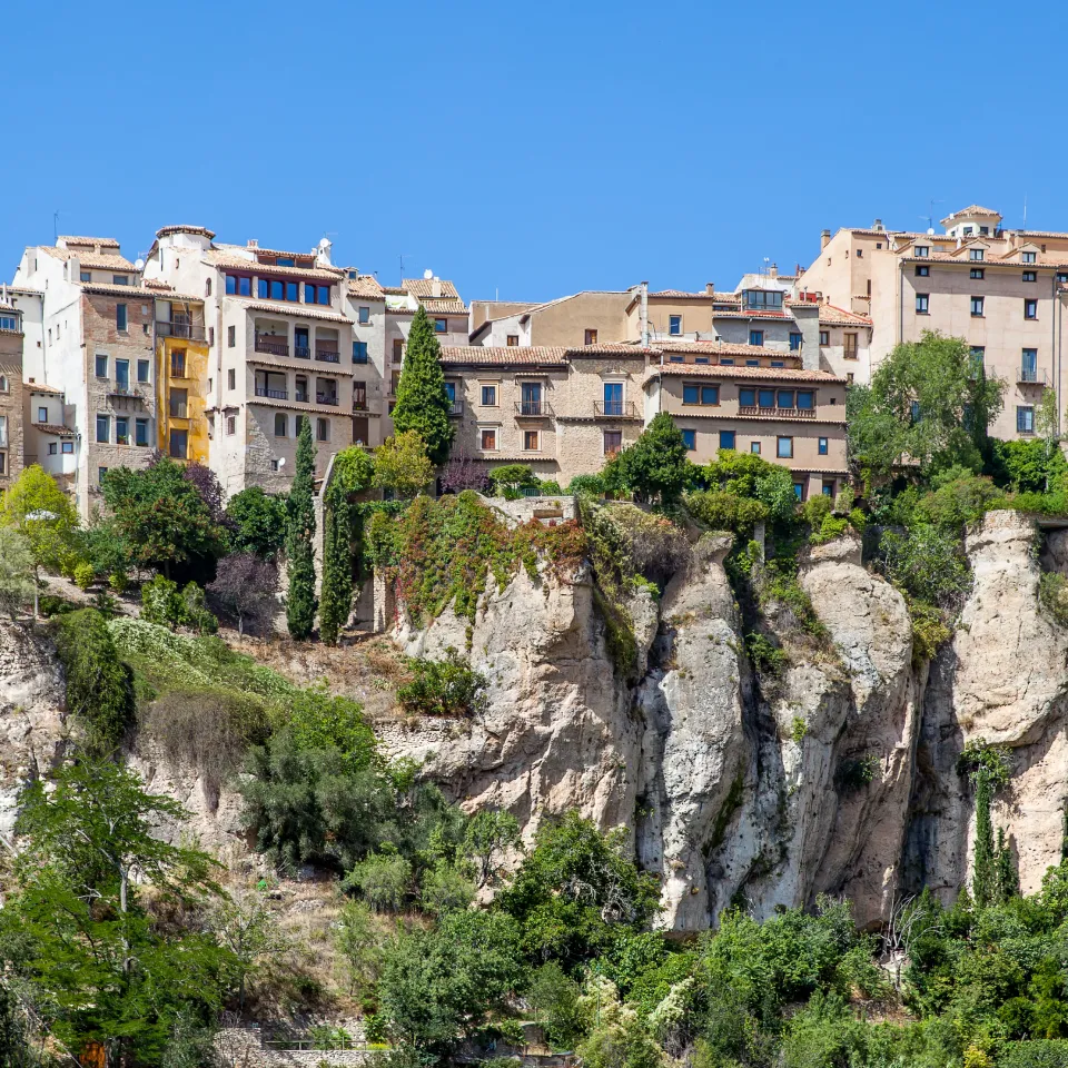 Casas blancas y edificios sobre acantilado rocoso con vegetaci&oacute;n y cielo azul