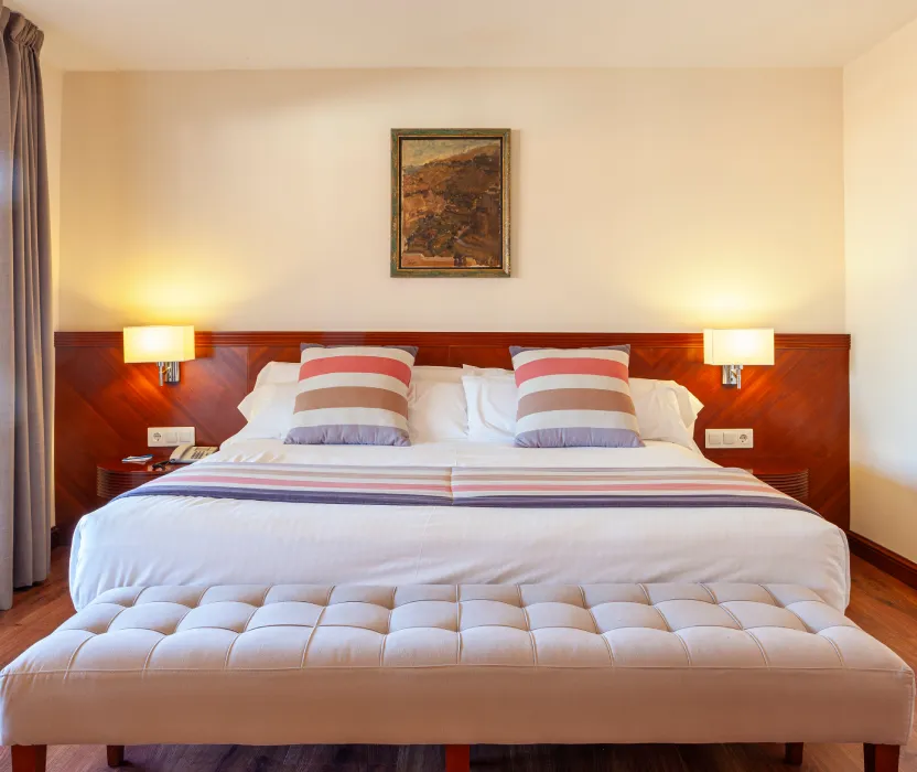 Dormitorio con cama doble, mesitas y l&aacute;mparas, y cuadro en la pared