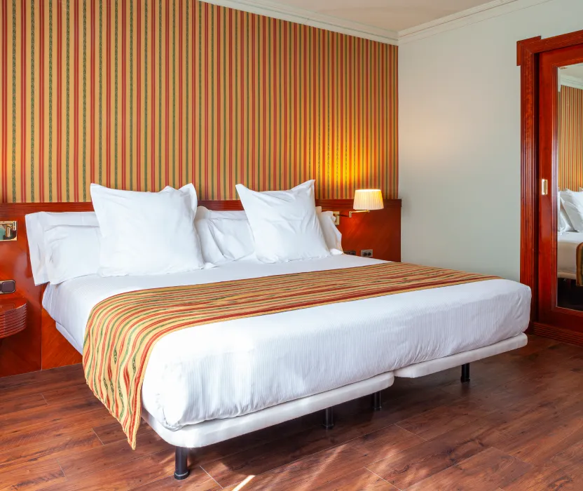 Habitaci&oacute;n de hotel con cama doble, l&aacute;mpara y pared con rayas.