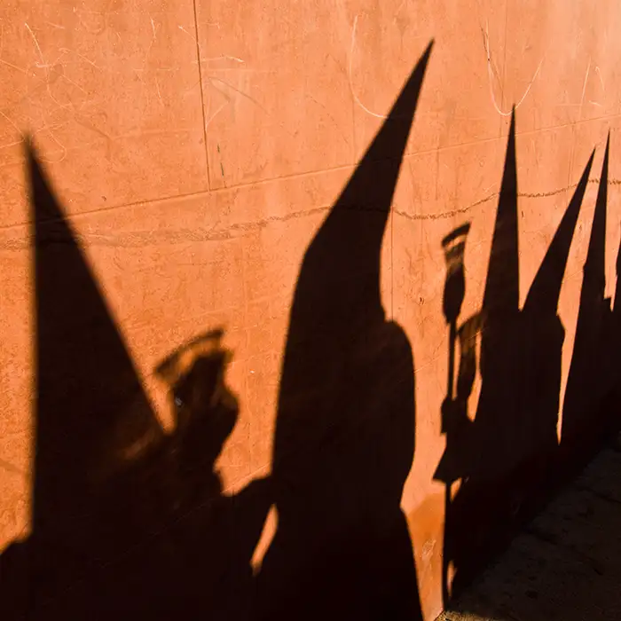 Sombras puntiagudas de personas y edificios sobre pared naranja al atardecer.