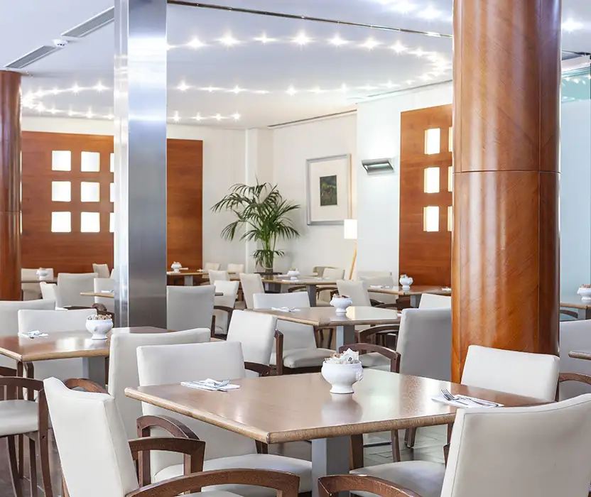 Comedor moderno con mesas de madera, sillas blancas y columnas de m&aacute;rmol.