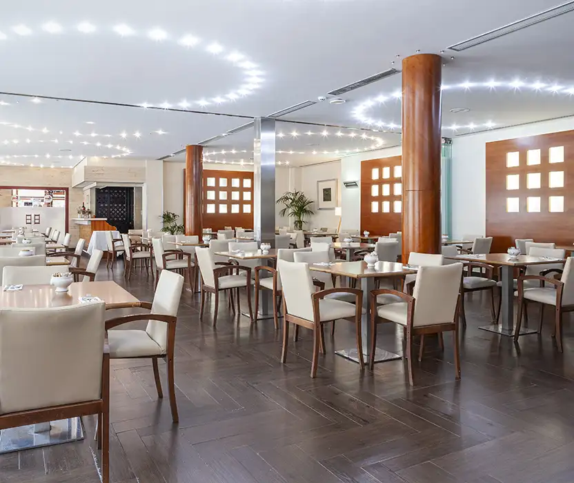Comedor moderno con mesas y sillas, columnas de madera y luces LED c&aacute;lidas.