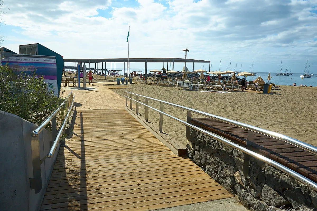 Pasarela de madera junto a la playa, sombrillas y sillas frente al mar