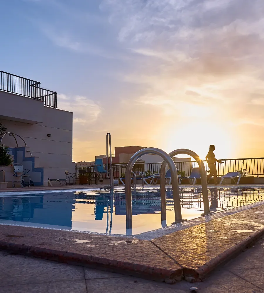 Piscina al atardecer, con persona saliendo y sol reflejado en el agua