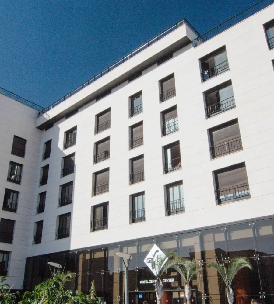 Fachada de edificio moderno blanco con ventanas y palmeras al frente.
