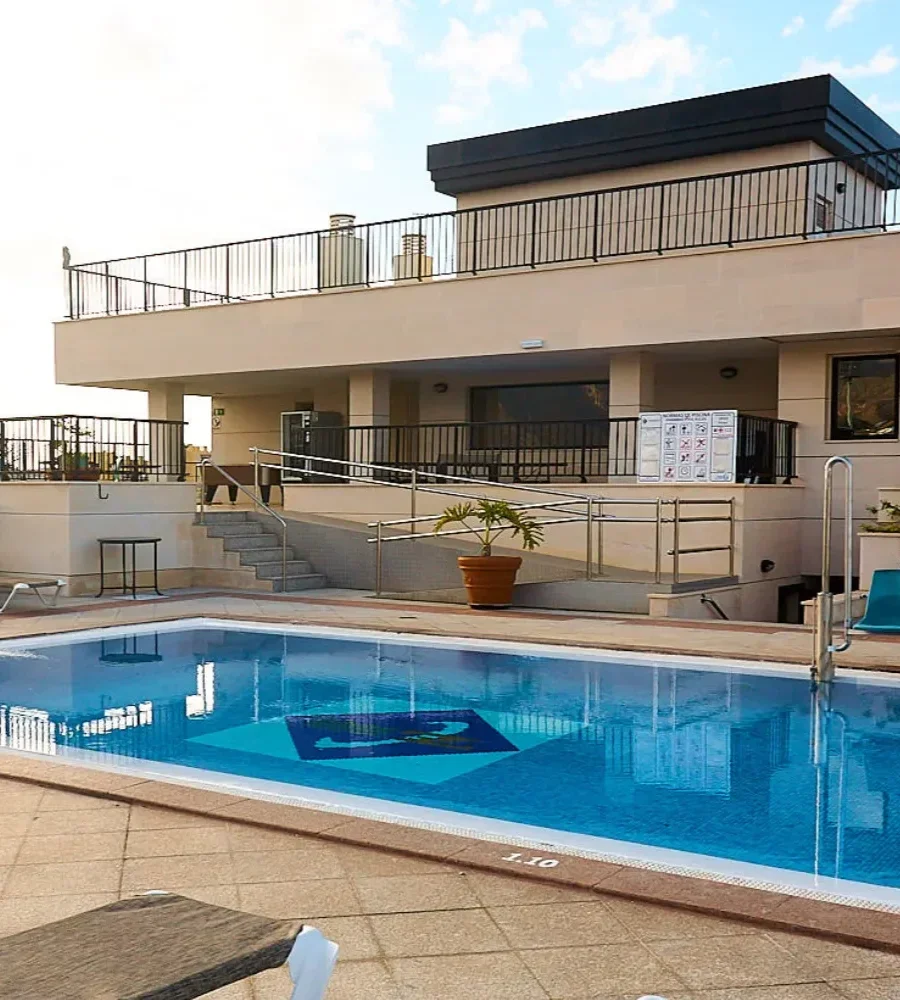 Piscina exterior junto a un edificio con terraza y barandillas met&aacute;licas