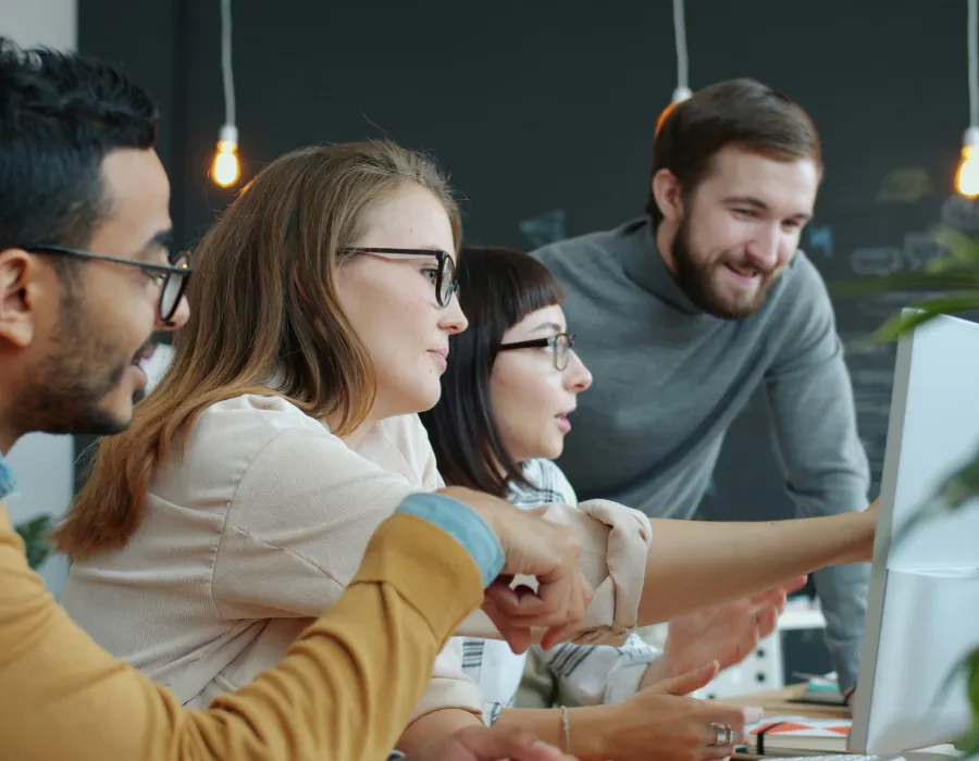 Equipo en oficina, personas trabajando y mirando una pantalla en reuniones.