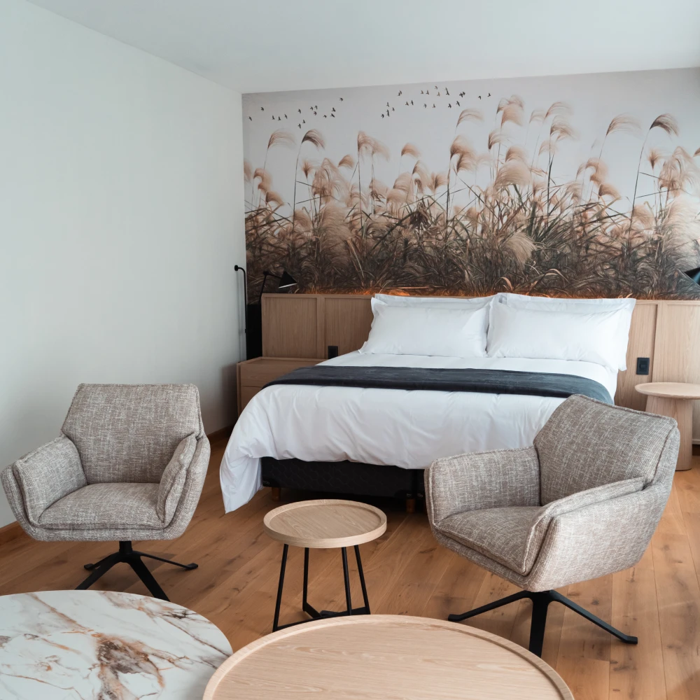 Dormitorio moderno con cama, sillones grises y mural de plumas en la pared
