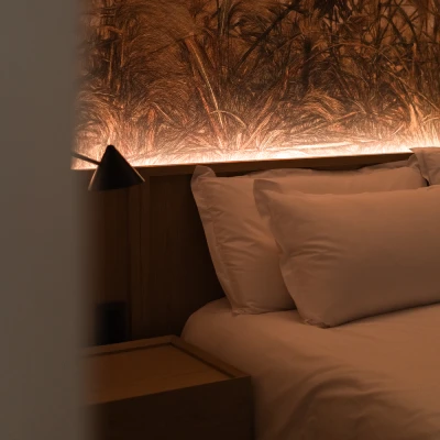 Cama con iluminaci&oacute;n c&aacute;lida y l&aacute;mpara, paredes de textura r&uacute;stica.