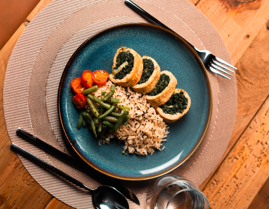 Plato azul con arroz, verduras y rollitos de espinaca en rebanadas.