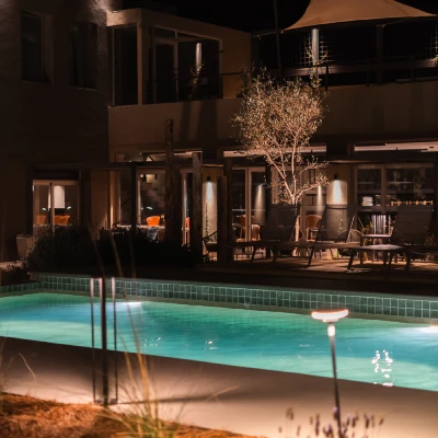 Piscina iluminada de noche junto a una casa con jard&iacute;n y luces c&aacute;lidas
