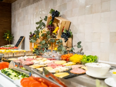 Mesa con s&aacute;ndwiches y vegetales en buffet, decorado con plantas y frutas.