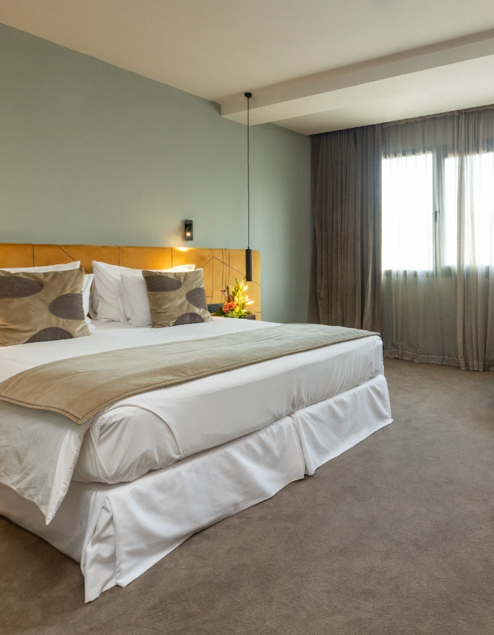Habitaci&oacute;n de hotel con cama doble, cortinas y luz c&aacute;lida junto a la ventana