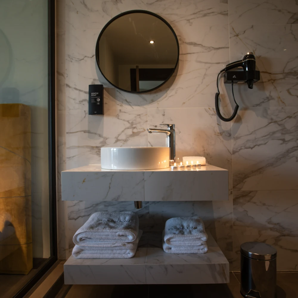 Lavabo moderno con espejo circular y toallas plegadas en ba&ntilde;o de m&aacute;rmol