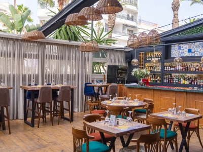 Terraza con mesas y sillas de madera, barra y jaulas decorativas.