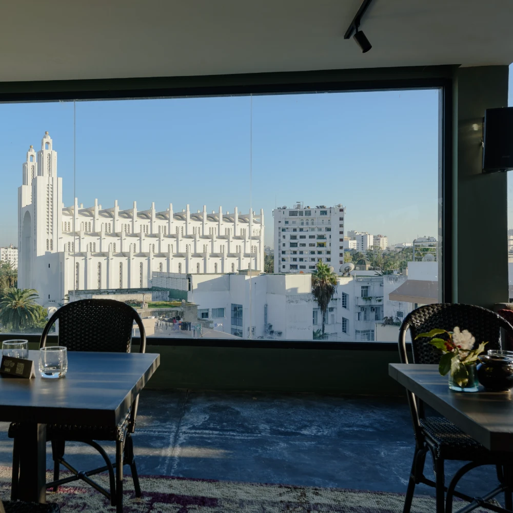 Vista urbana desde ventana: sillas y mesa, edificios blancos al fondo.