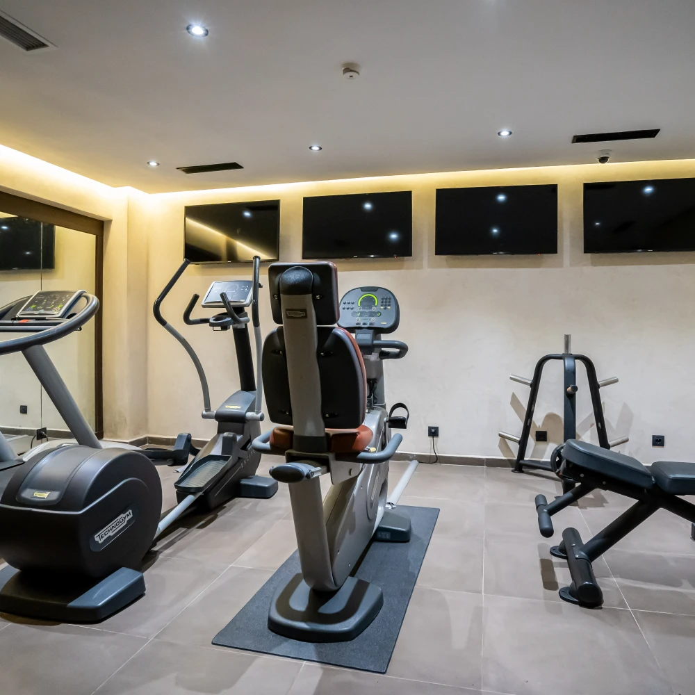 Gimnasio con m&aacute;quinas cardio y pesas, pantallas LED en pared.