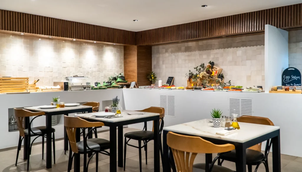 Buffet de desayuno con estaci&oacute;n de huevos, mesas y sillas en cocina moderna