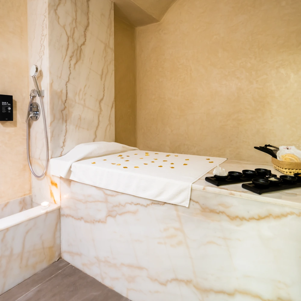 Ba&ntilde;era de m&aacute;rmol con accesorios y toalla sobre el borde en un cuarto.