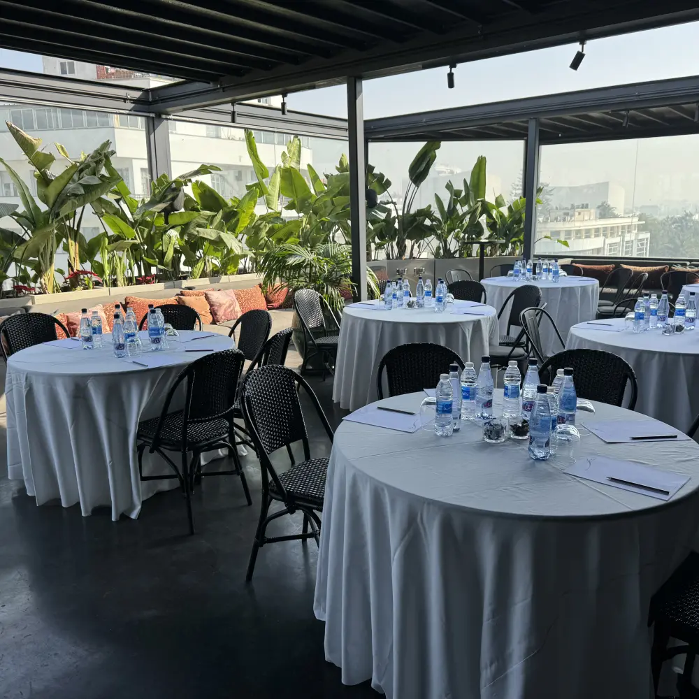 Mesa de banquete con botellas de agua y sillas en terraza cerrada con plantas