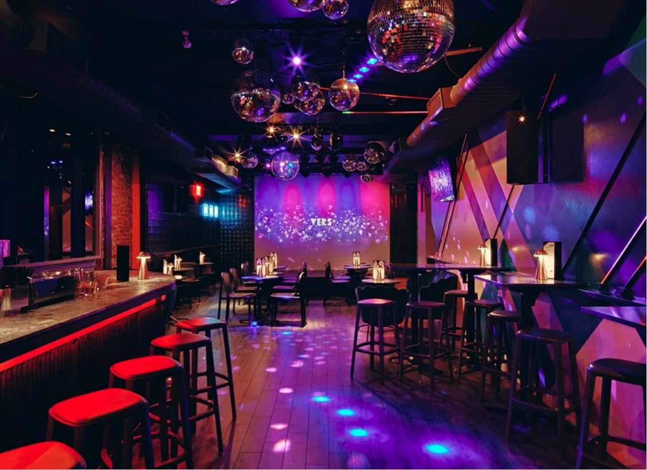 Sala de fiesta con mesas y luces moradas, rojo y bola de espejos