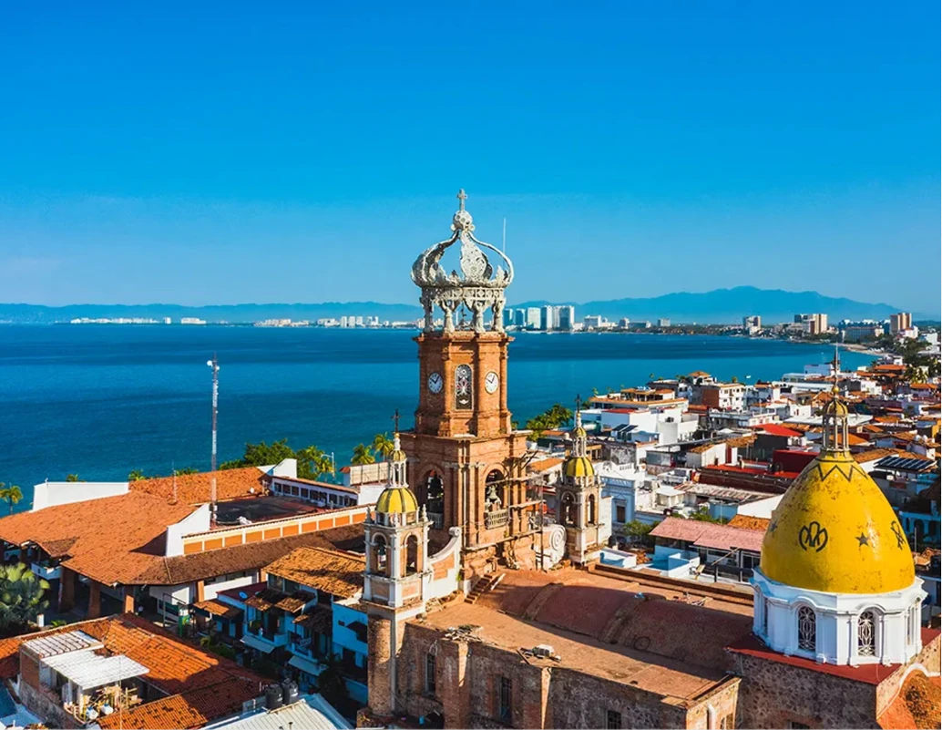 Iglesia colonial con c&uacute;pula amarilla y vista al mar y ciudad al fondo.