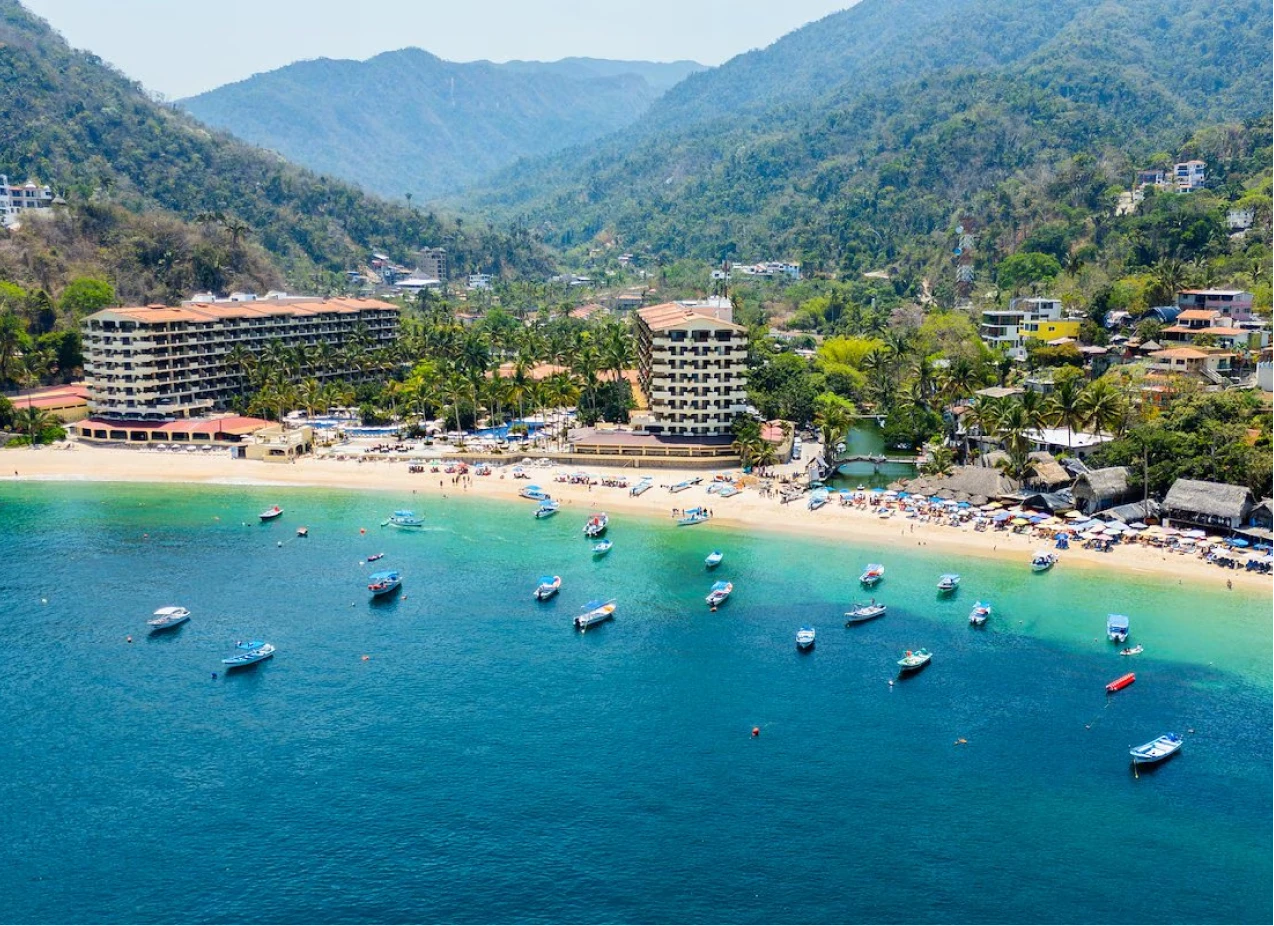 Playa tropical con botes, hotel junto a la costa y monta&ntilde;as al fondo