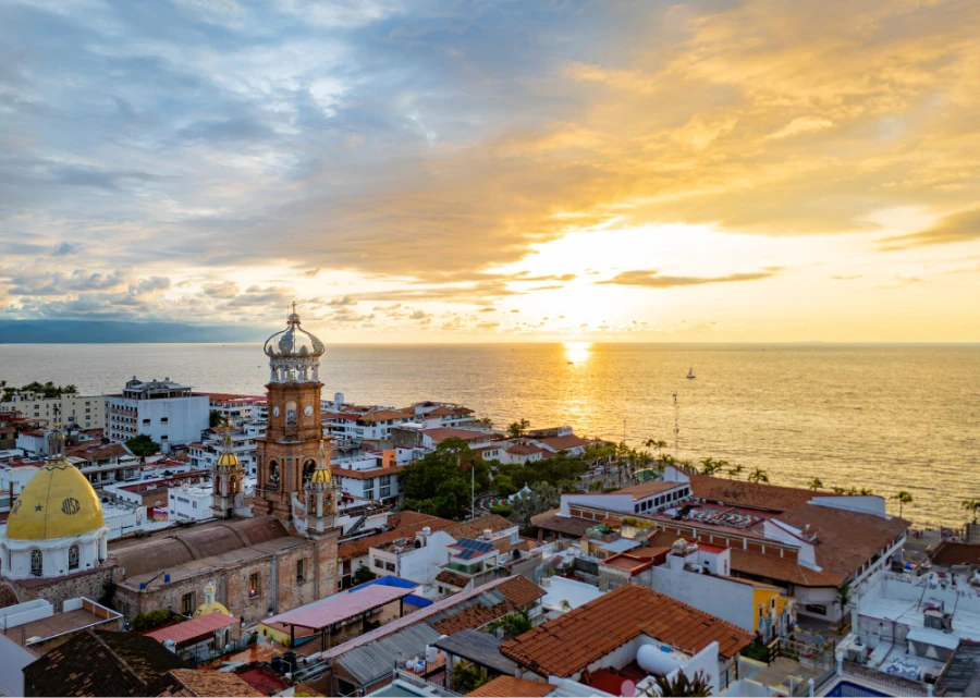 Puesta de sol sobre ciudad costera con reloj y campanario iluminado
